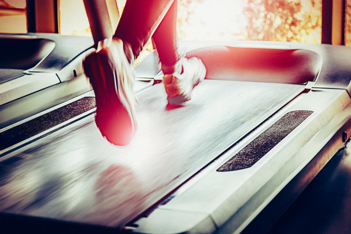 Feet shown running on treadmill, indoor gym