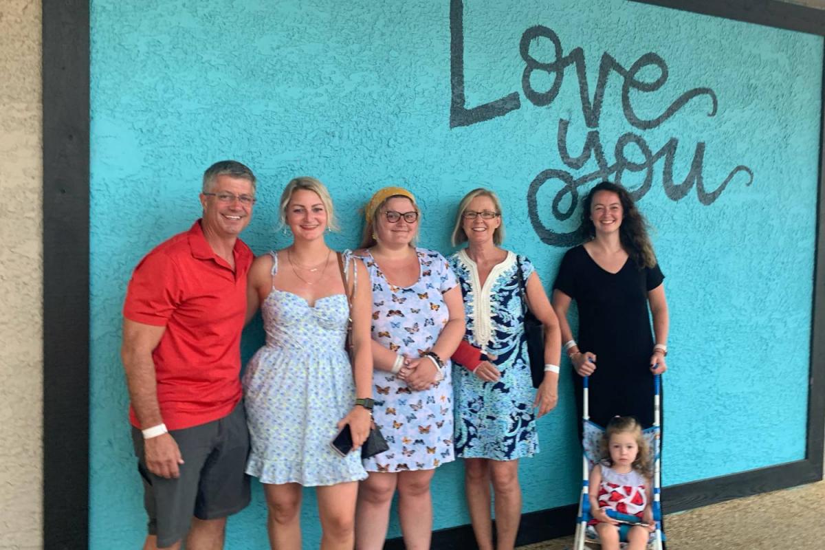 A family poses for a casual portrait in front of a teal wall featuring the painted words, "Love you."